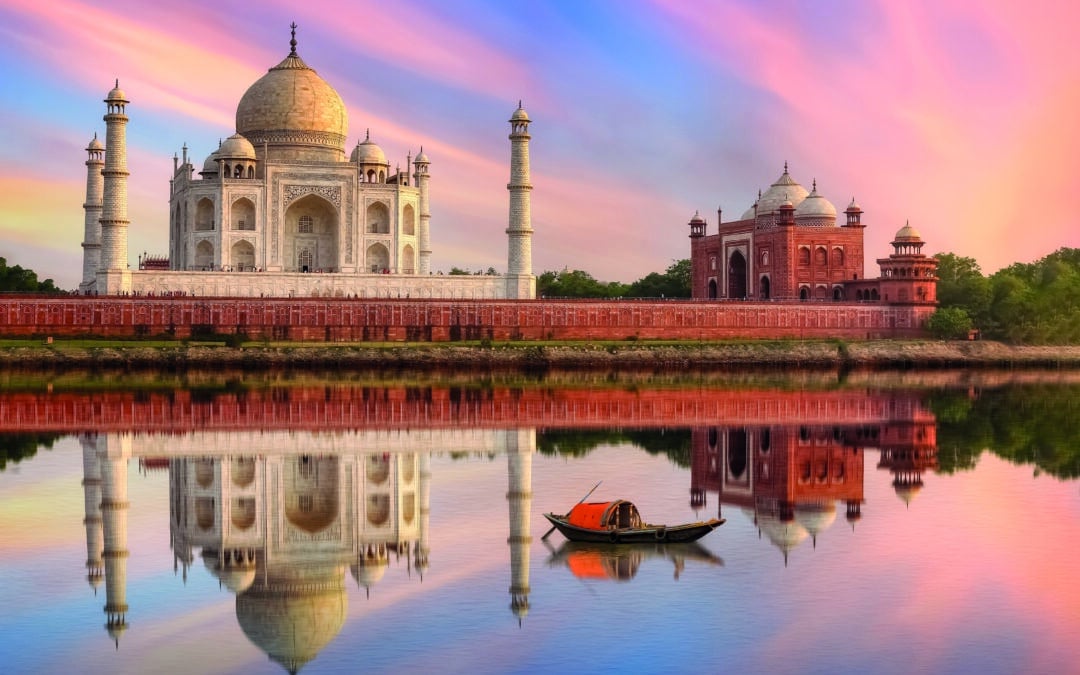 Taj Mahal Agra India at sunset on the banks of river Yamuna with moody sunset sky and view of wooden boat used for tourist ride on the river